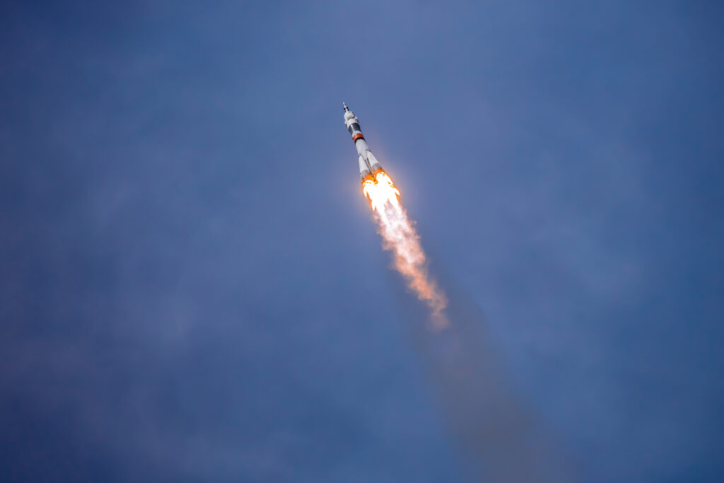 Rocket launching upward with bright exhaust flames and smoke trail against clear blue sky