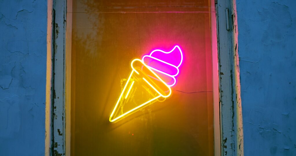 Pink and yellow neon ice cream cone sign illuminated in a storefront window