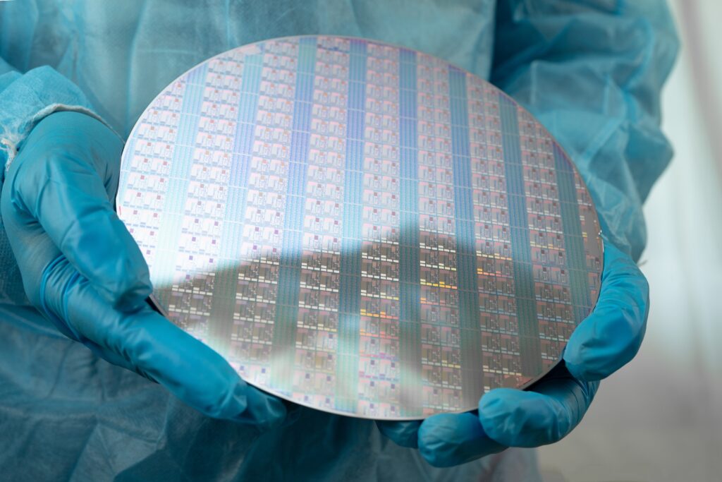 Gloved technician holding a finished silicon wafer in a semiconductor cleanroom