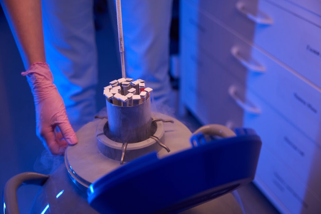 Gloved technician lifting sample canisters from a liquid nitrogen storage dewar with vapor rising from the neck