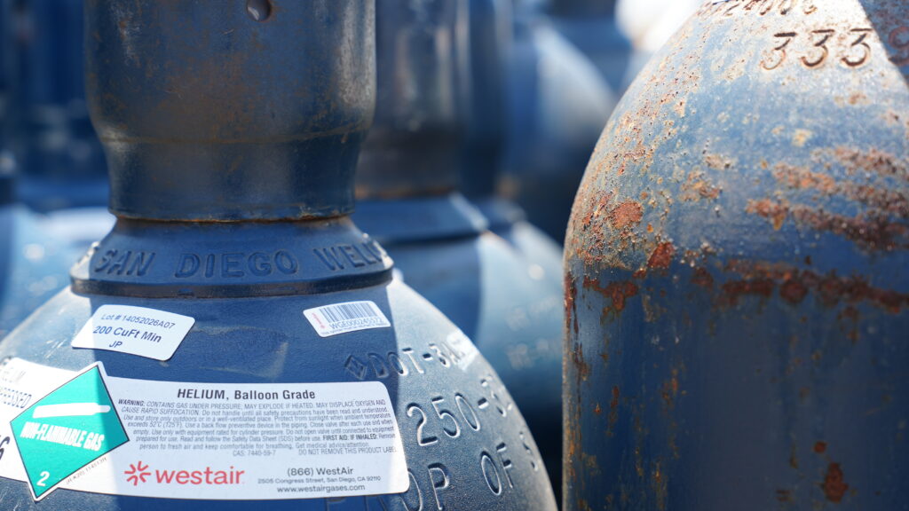 A blue WestAir compressed helium cylinder with a non-flammable gas label and safety warnings