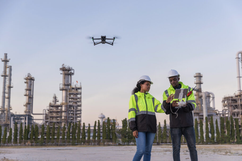 Two workers in high-visibility jackets operating an inspection drone outside a gas processing facility