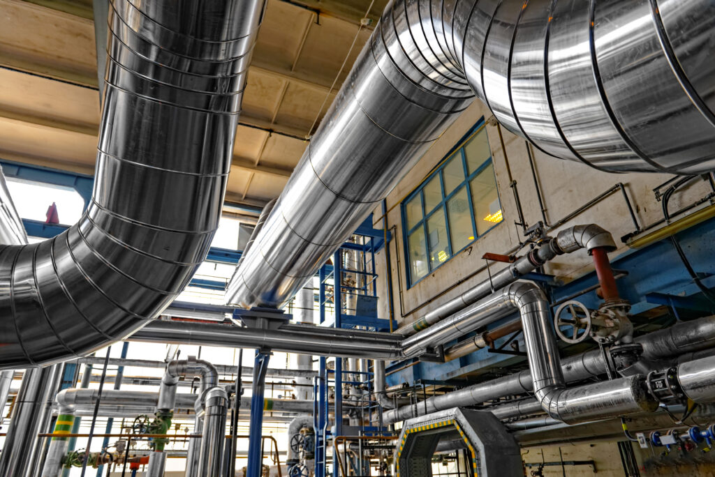 Insulated process piping and valves running along the ceiling of a factory interior