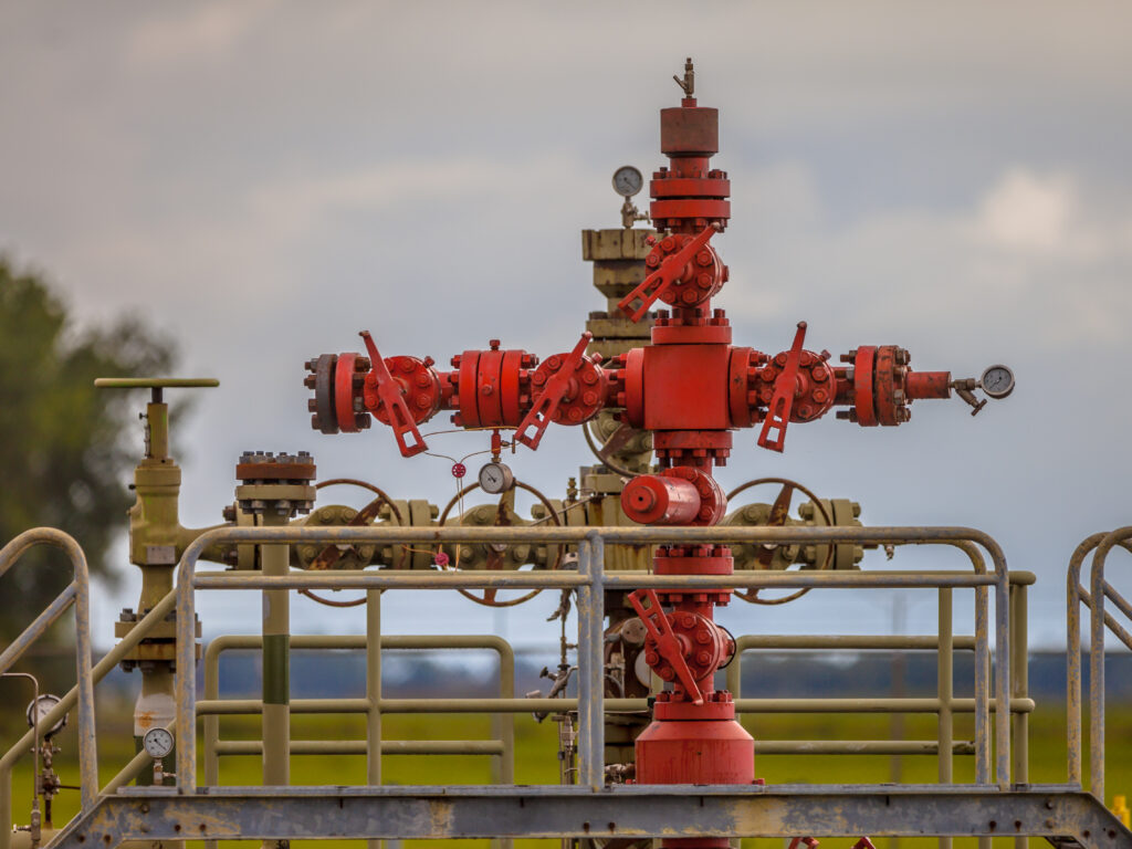 Red and tan wellhead valve assembly with pressure gauges in a rural field